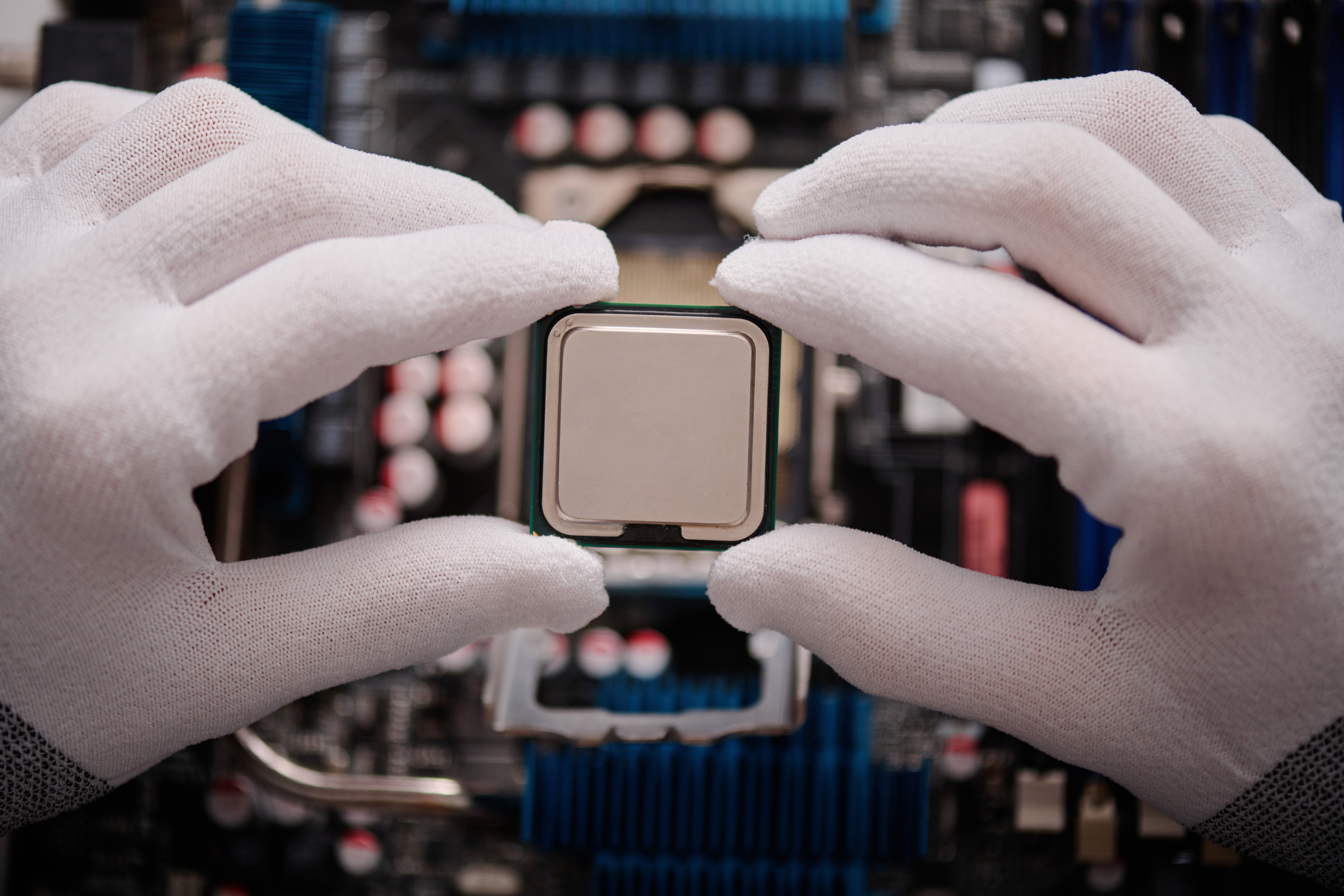 Gloved Hands of Technician Inserting Microchip Into Computer Motherboard A close-up shot reveals hands wearing white gloves carefully holding a computer processor